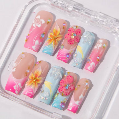 Decorative false nails with floral designs and rhinestones in a clear display case.