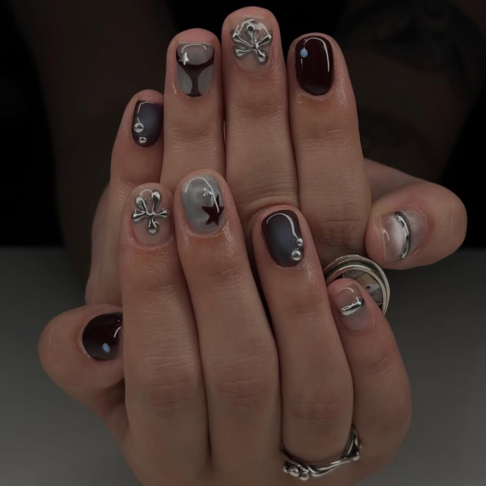 Close-up of a hand with decorative nail art and rings on a dark background