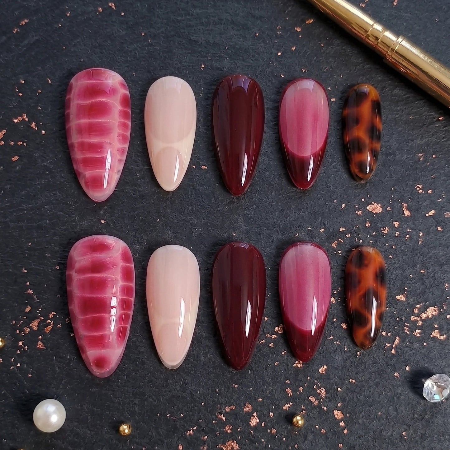 Collection of nail art designs on a dark surface with a brush and decorative elements.