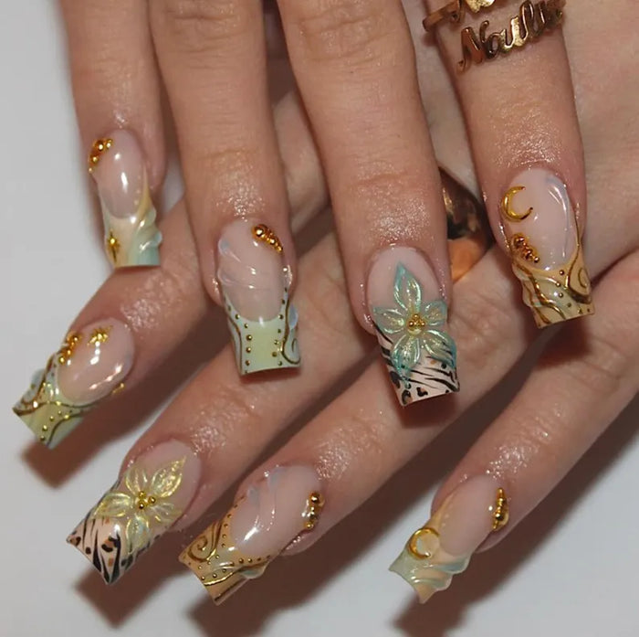Close-up of a hand with intricately designed nails featuring gold, black, and white patterns on a white background.